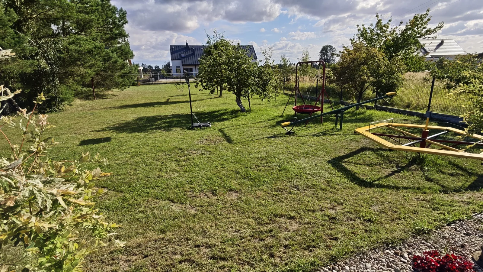 Plac zabaw dla dzieci na terenie U Marianny w Mikoszewie — huśtawki, karuzela i huśtawka wagowa na trawie